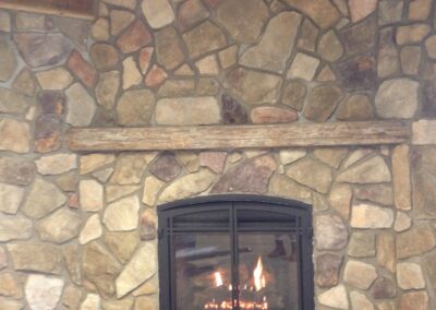 gas fireplace with light chunky stone surround and distressed wood mantel