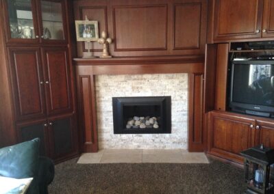 small gas fireplace with small round stone log set, glass doors, and wooden mantel and surround