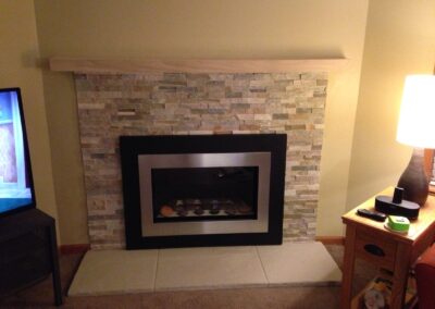 gas fireplace with round stone gas log set, light stone surround, and light wood mantel