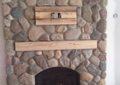 gas fireplace with chunky stone surround and light wood mantel