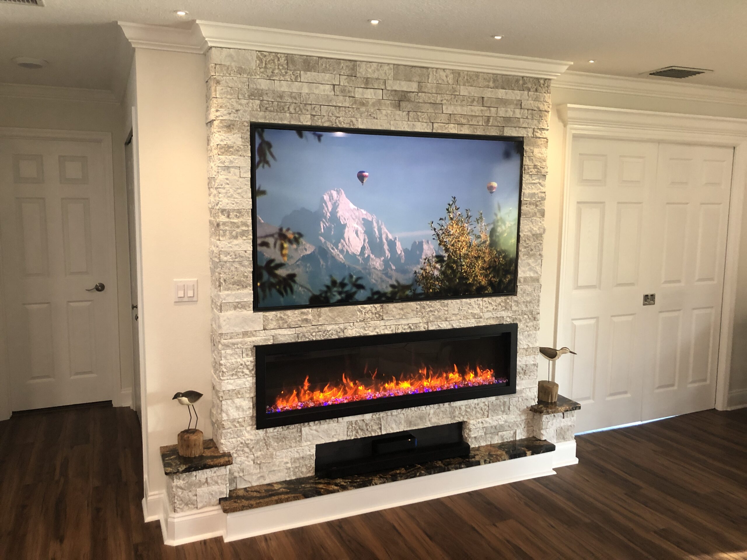 Electric fireplace in living room with custom light stone surround and tv mount